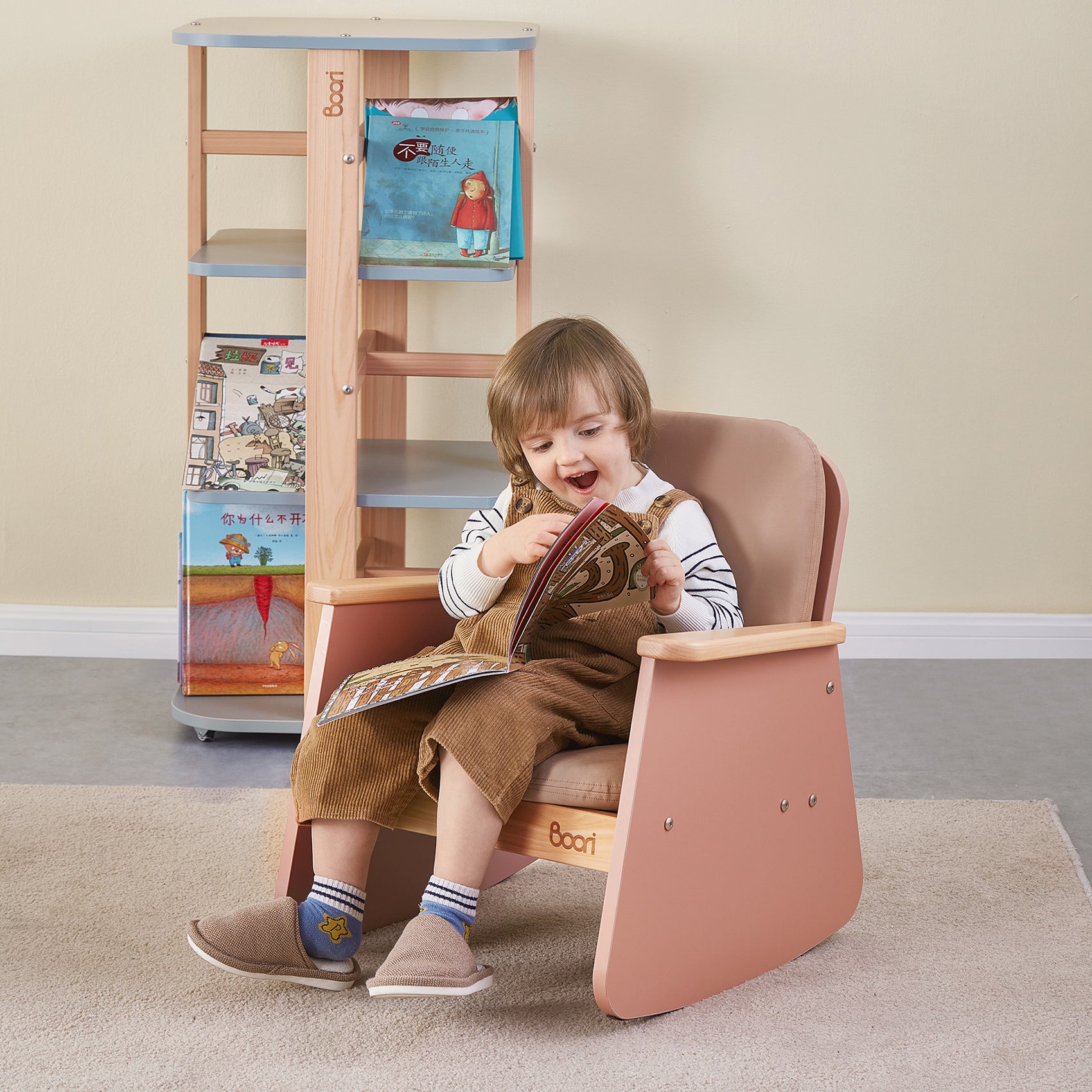 Young girl in overalls reads a book while sitting in a pink child-sized rocking chair